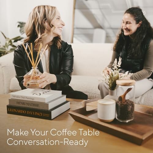 Two women talking on a sofa with coffee table books and decor.